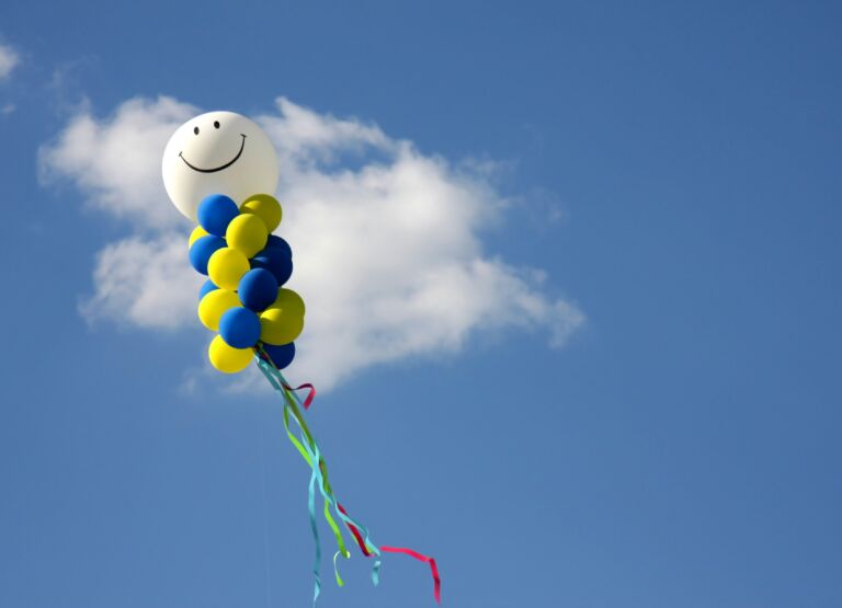 Balon cu chip zâmbitor și baloane colorate pe cer, simbol al fericirii și optimismului